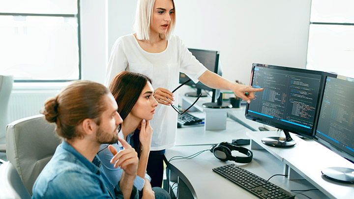 Three people reviewing some computer code on a computer screen.
